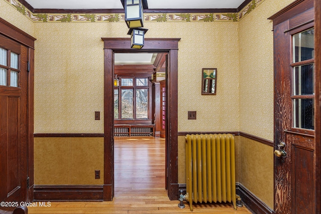 hall with wood finished floors, wainscoting, radiator heating unit, and wallpapered walls