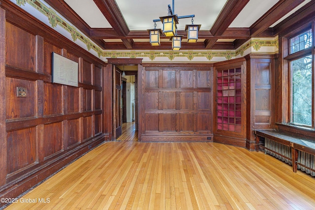 spare room with radiator, coffered ceiling, light wood finished floors, wood walls, and beamed ceiling