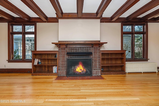 unfurnished living room with a tile fireplace, beamed ceiling, radiator, and wood finished floors