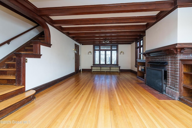 unfurnished living room with stairs, beam ceiling, a brick fireplace, and wood finished floors