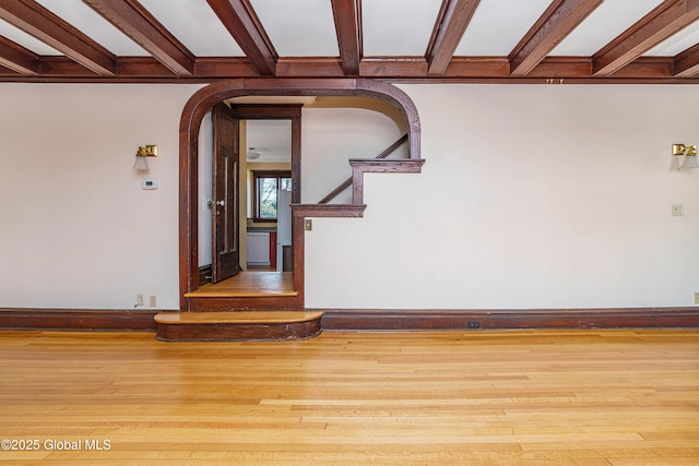 unfurnished room with beamed ceiling, arched walkways, baseboards, and wood finished floors