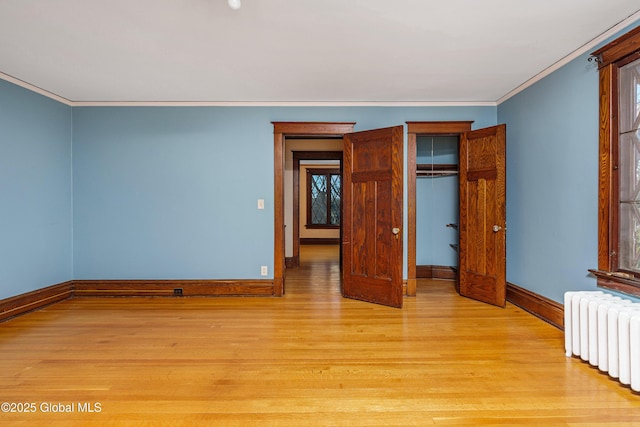 unfurnished bedroom with crown molding, baseboards, light wood-type flooring, radiator heating unit, and a closet