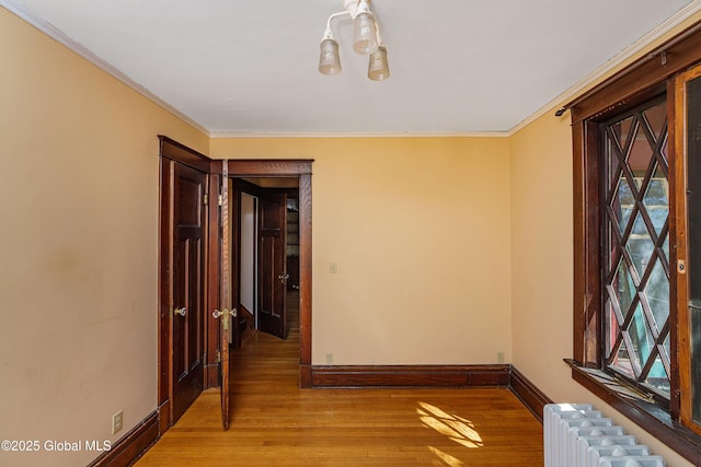 corridor featuring crown molding, baseboards, a chandelier, radiator heating unit, and wood finished floors