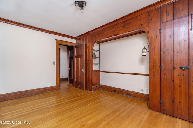 empty room featuring arched walkways, baseboards, crown molding, and light wood-style floors