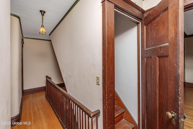 hallway with an upstairs landing, crown molding, baseboards, and wood finished floors