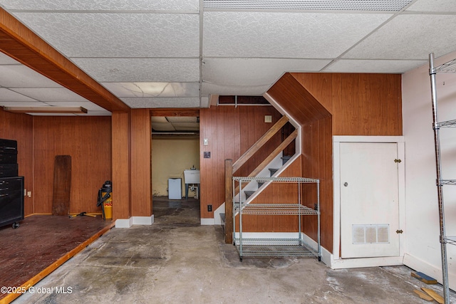 basement featuring stairs, wooden walls, visible vents, and a drop ceiling