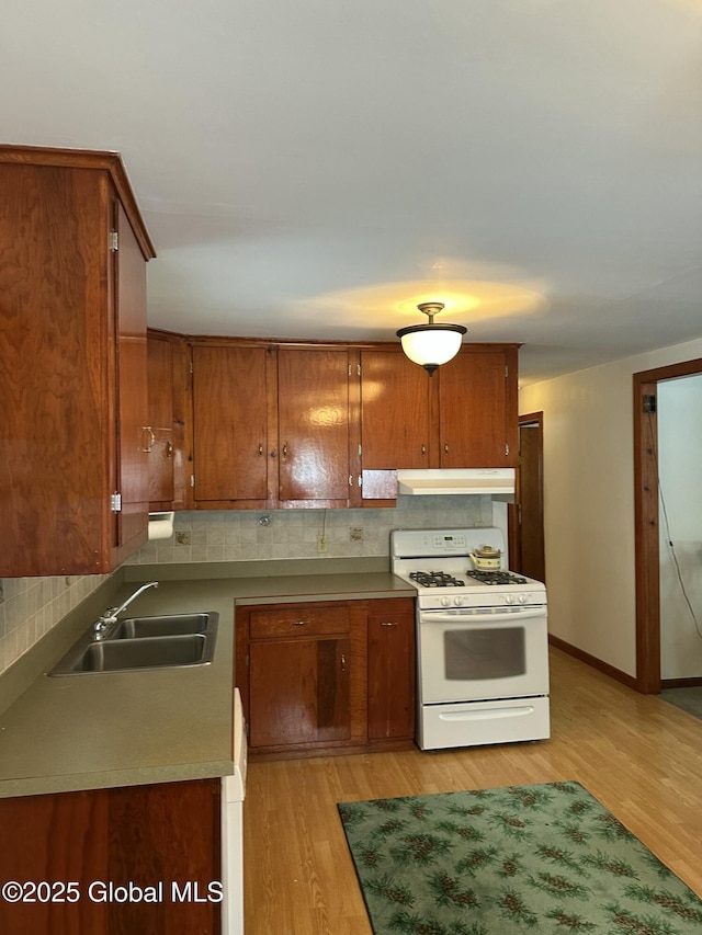 kitchen with under cabinet range hood, a sink, white gas range oven, light wood finished floors, and brown cabinetry