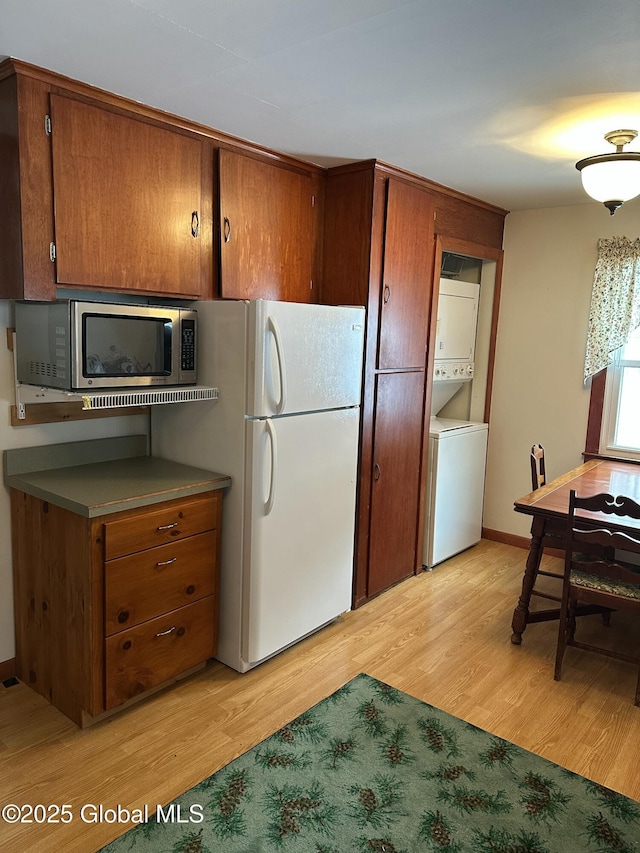 kitchen featuring stacked washer and dryer, freestanding refrigerator, brown cabinetry, and stainless steel microwave