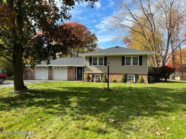 tri-level home featuring driveway, an attached garage, a front lawn, and brick siding