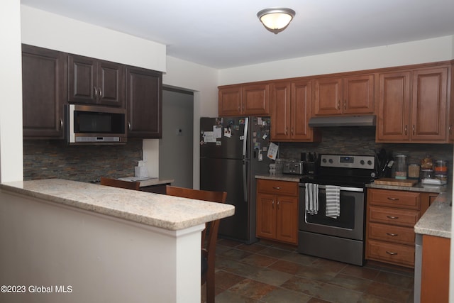 kitchen featuring light stone countertops, under cabinet range hood, appliances with stainless steel finishes, and decorative backsplash