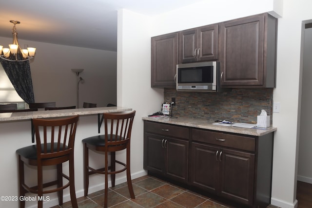 kitchen with a chandelier, a kitchen breakfast bar, dark brown cabinets, backsplash, and stainless steel microwave