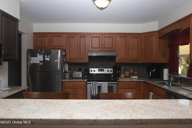 kitchen featuring appliances with stainless steel finishes, light stone counters, a sink, under cabinet range hood, and backsplash