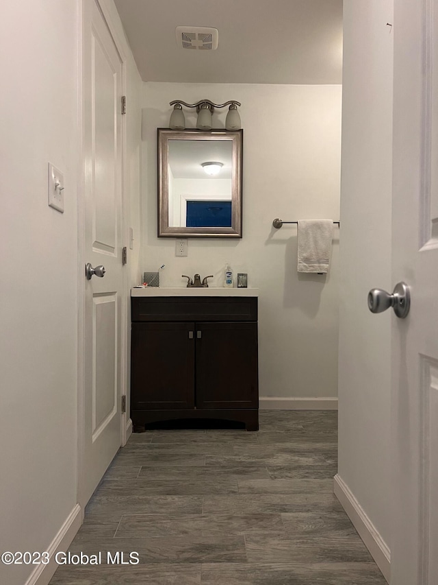 bathroom with visible vents, vanity, baseboards, and wood finished floors