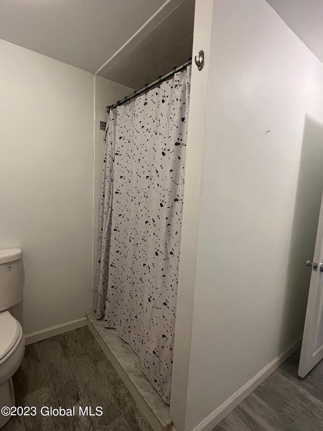 bathroom featuring toilet, a shower with curtain, baseboards, and wood finished floors