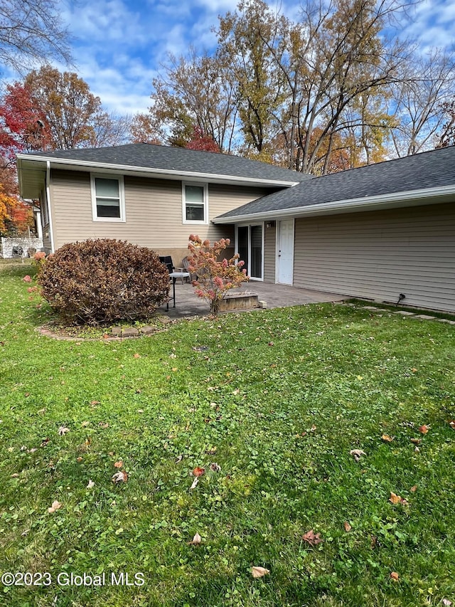 rear view of house with a patio area, a lawn, and roof with shingles