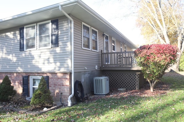 view of side of property with central air condition unit, brick siding, a deck, and a yard