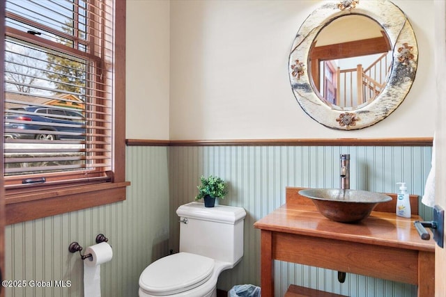 half bath with toilet, a wainscoted wall, and a sink