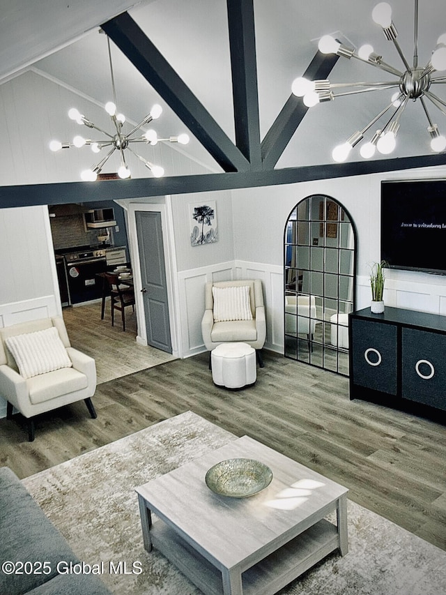 living area featuring lofted ceiling with beams, a decorative wall, wood finished floors, and a notable chandelier