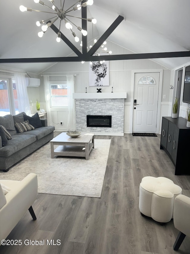 living room featuring lofted ceiling with beams, a chandelier, wood finished floors, and a stone fireplace