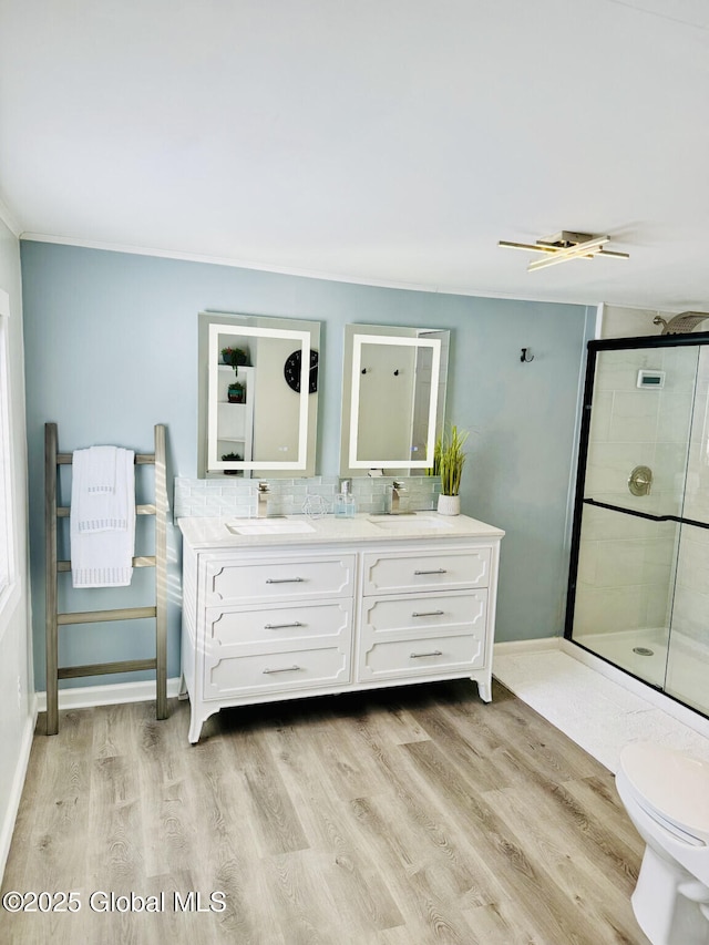 full bath featuring a sink, wood finished floors, a shower stall, double vanity, and tasteful backsplash