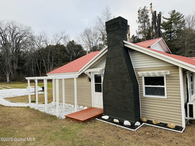 view of side of home featuring metal roof, a lawn, and a chimney