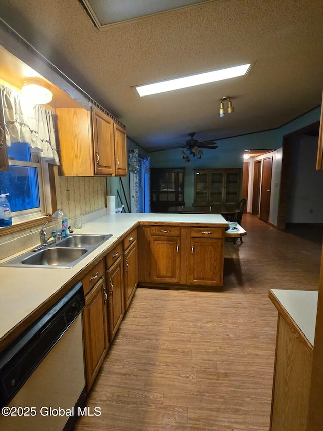 kitchen featuring dishwashing machine, brown cabinets, a peninsula, light countertops, and a sink