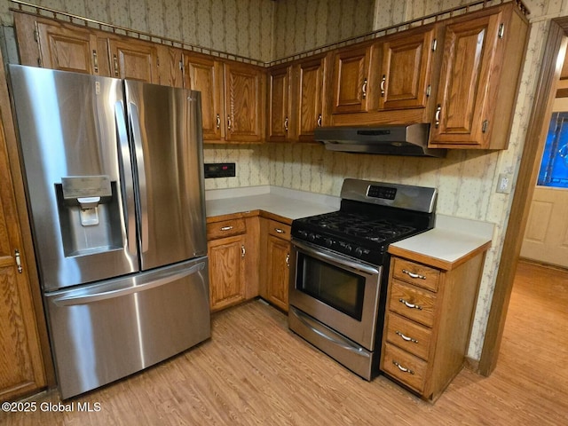 kitchen with under cabinet range hood, light countertops, appliances with stainless steel finishes, light wood finished floors, and brown cabinetry