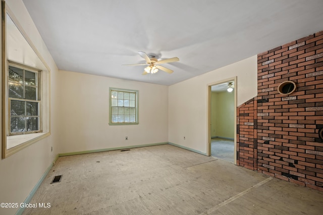 empty room featuring visible vents, ceiling fan, and brick wall