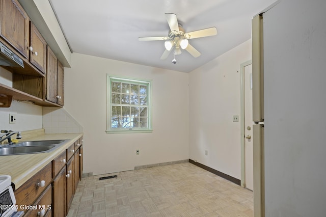 kitchen featuring baseboards, brown cabinetry, ceiling fan, light countertops, and a sink