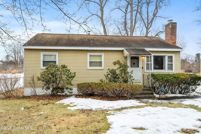 view of front of house with a lawn, a chimney, and a shingled roof