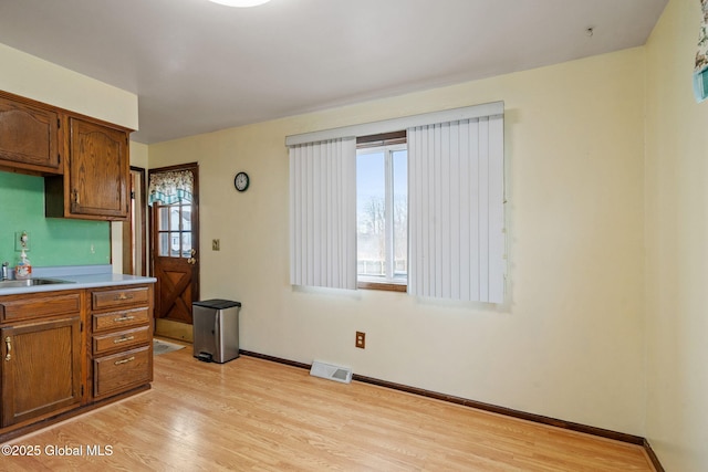 kitchen with baseboards, visible vents, light wood-style flooring, a sink, and light countertops