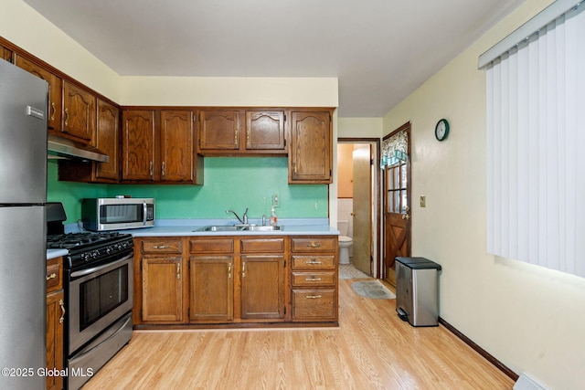 kitchen with a sink, under cabinet range hood, stainless steel appliances, light wood-style floors, and light countertops