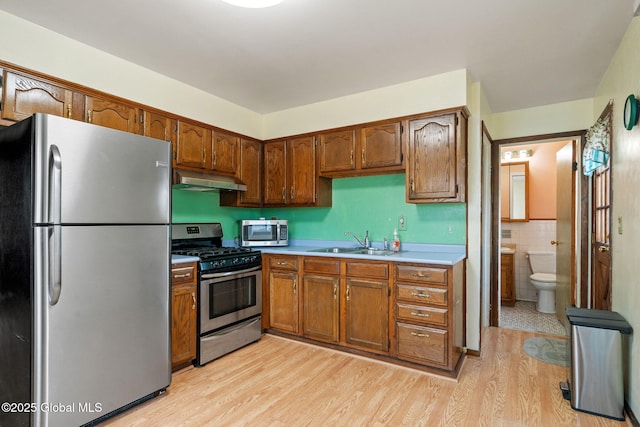 kitchen with a sink, under cabinet range hood, tile walls, appliances with stainless steel finishes, and light countertops