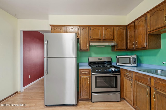 kitchen featuring stainless steel appliances, light wood-style floors, range hood, and light countertops