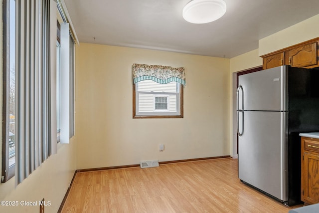 kitchen with brown cabinetry, visible vents, light wood finished floors, baseboards, and freestanding refrigerator