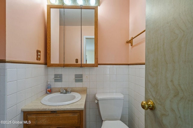 bathroom featuring vanity, tile walls, toilet, and a wainscoted wall