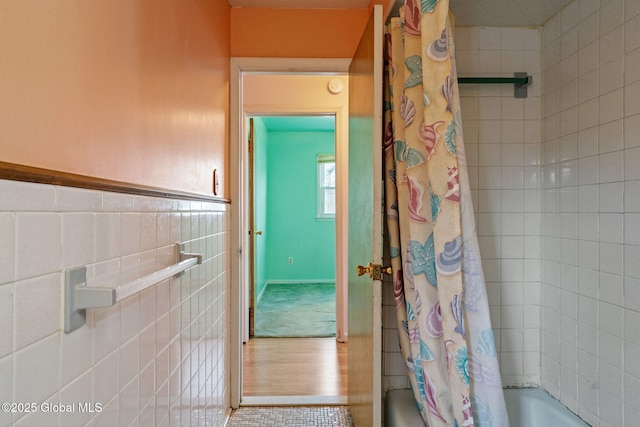 full bath featuring tile walls, shower / tub combo, and a wainscoted wall