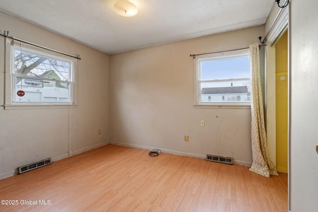 unfurnished room featuring light wood-type flooring, visible vents, and a wealth of natural light