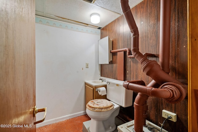 half bath featuring wooden walls, baseboards, toilet, a textured ceiling, and a sink