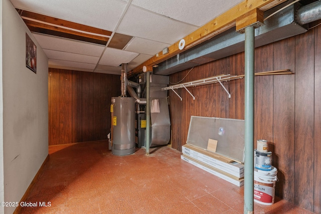 finished below grade area with a paneled ceiling, water heater, and wood walls