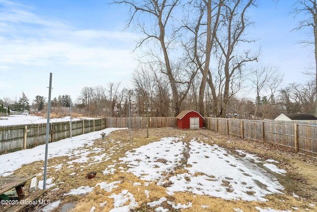 snowy yard featuring an outbuilding, a fenced backyard, and a shed