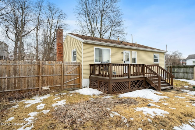 snow covered back of property with a deck, fence private yard, and a chimney