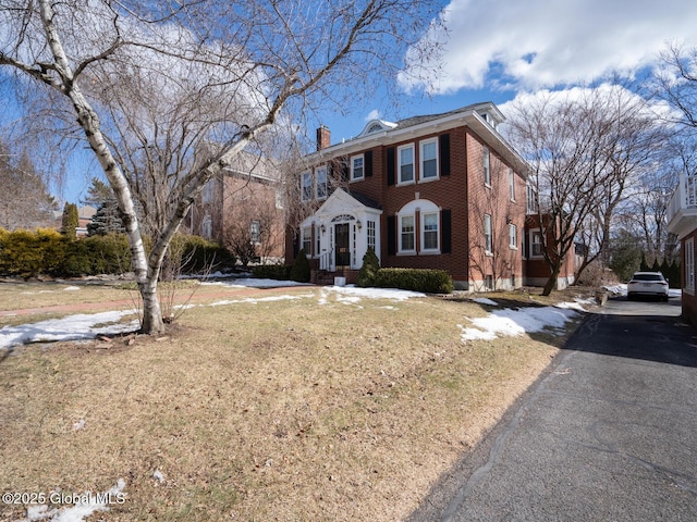 view of front facade featuring a front yard, a chimney, and brick siding