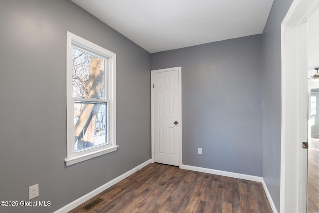 unfurnished room with dark wood-type flooring, visible vents, and baseboards