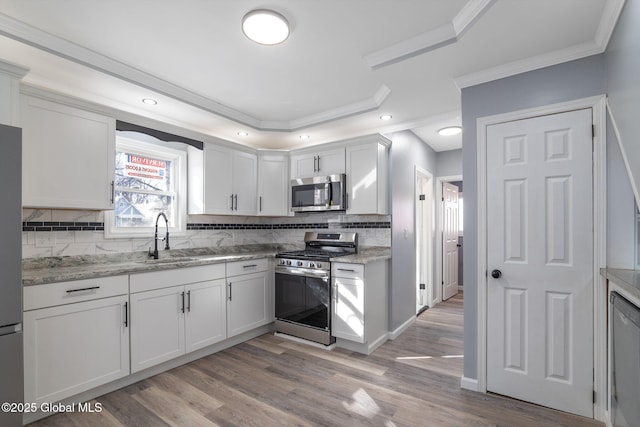 kitchen featuring appliances with stainless steel finishes, backsplash, crown molding, light wood-type flooring, and a sink