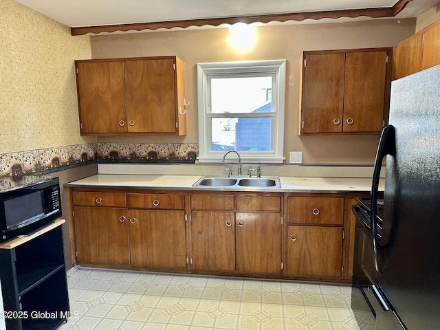 kitchen featuring black appliances, a sink, brown cabinetry, light countertops, and light floors