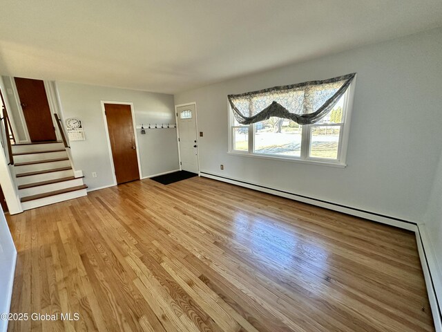 unfurnished living room with stairway, a baseboard radiator, and wood finished floors