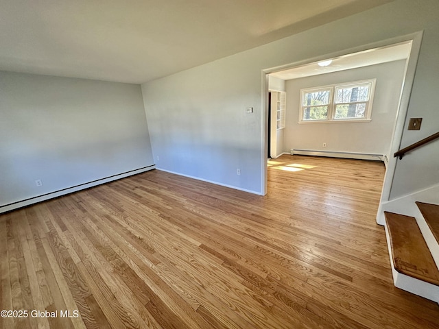 empty room featuring a baseboard radiator, wood finished floors, and stairway