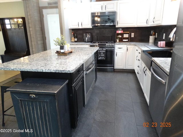 kitchen featuring appliances with stainless steel finishes, white cabinets, a kitchen island, dark cabinets, and a kitchen breakfast bar