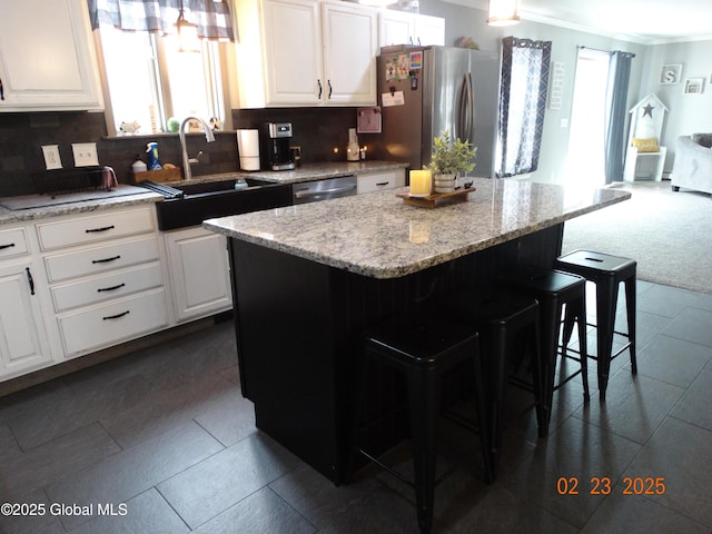 kitchen with a center island, stainless steel appliances, white cabinetry, a sink, and a kitchen bar